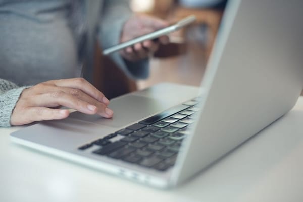 A woman sitting at a desk with a laptop and her smartphone shopping on social media