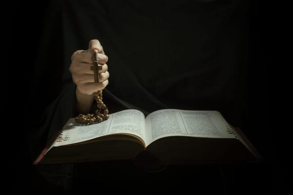 Closeup of Hands holding rosary beads and cross while reading bible