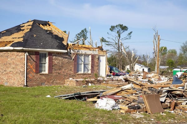 Home torn apart by tornado damage with debris in yard